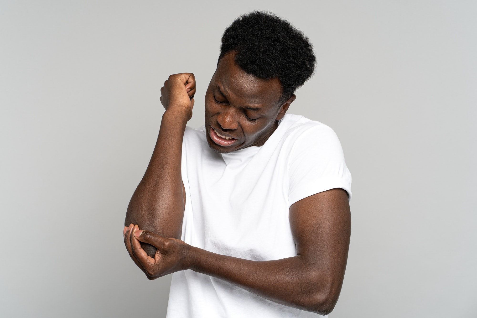 Unhappy Black man in t-shirt suffers her elbow joint pain or arm bone osteoporosis, pinched nerve