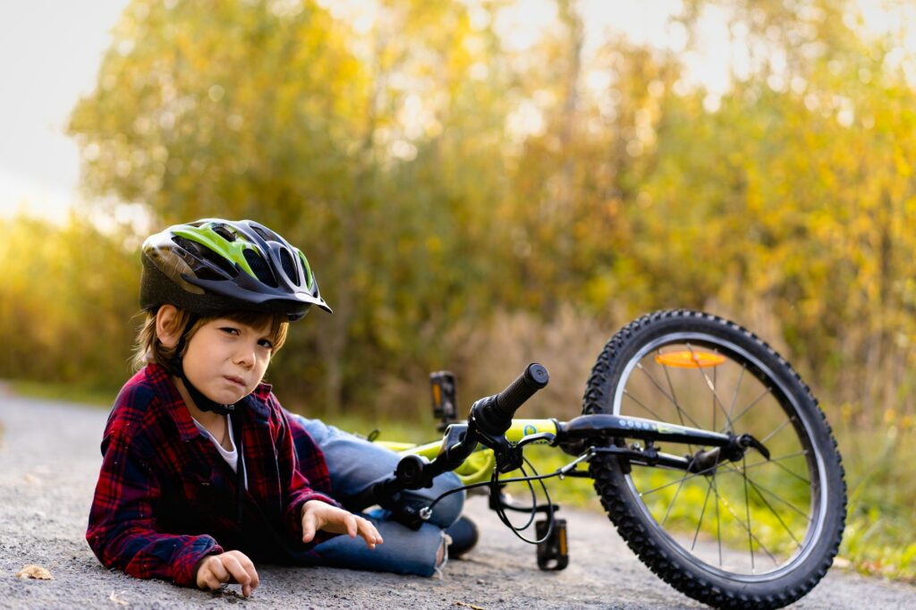 A little boy in a protective helmet fell off his bicycle. Injury, pain, bruised, abrasure.