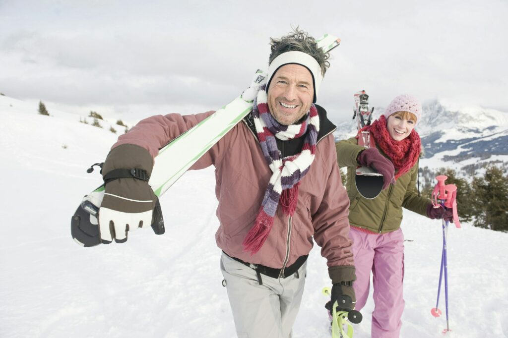 Italy, South Tyrol, Seiseralm, Couple carrying skis, smiling, portrait