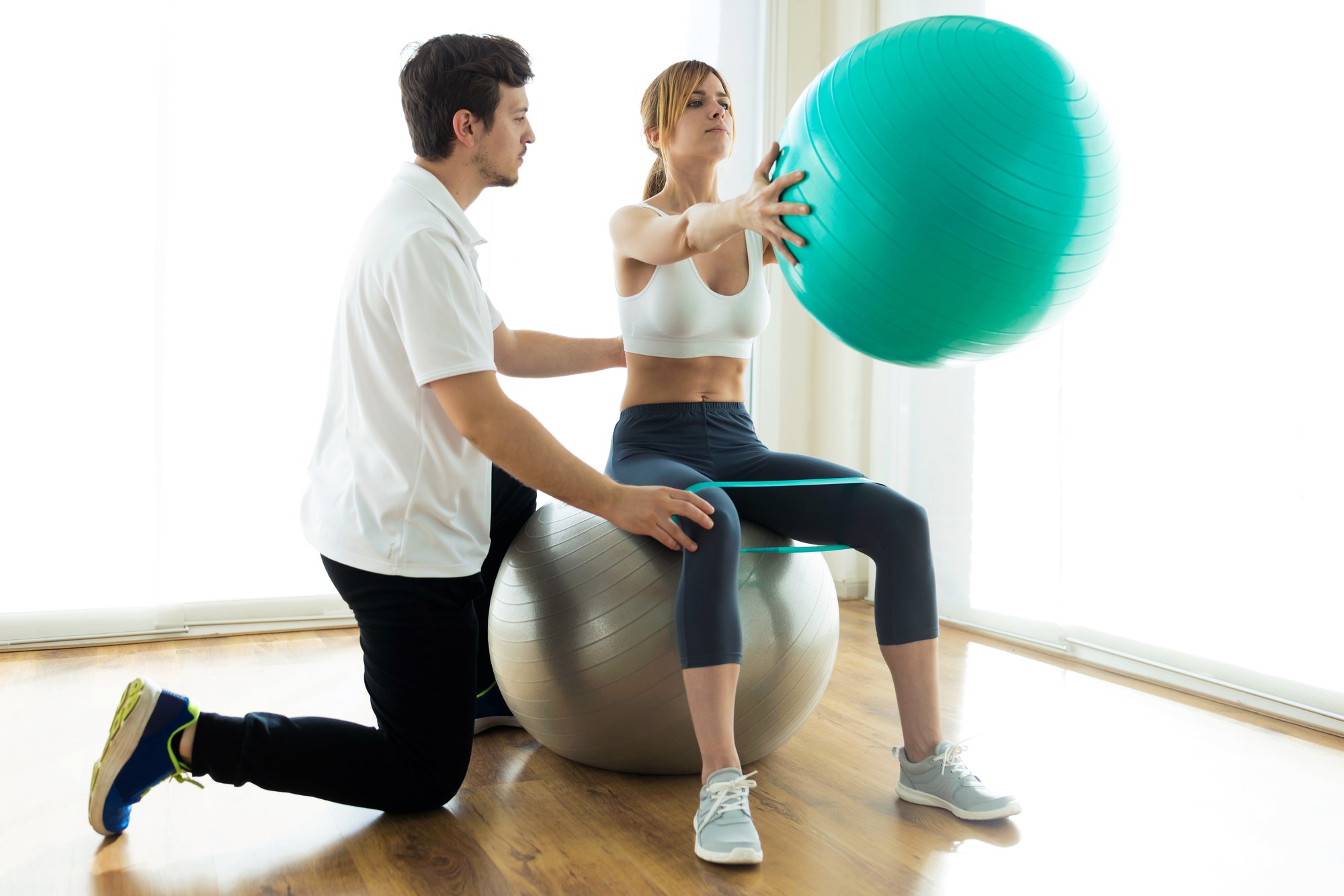 Physiotherapist helping patient to do exercise on fitness ball in physio room.