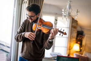 Young caucasian man playing violin at home. Hobby quality time happiness concept.