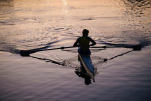 Young man rowing on river at sunset